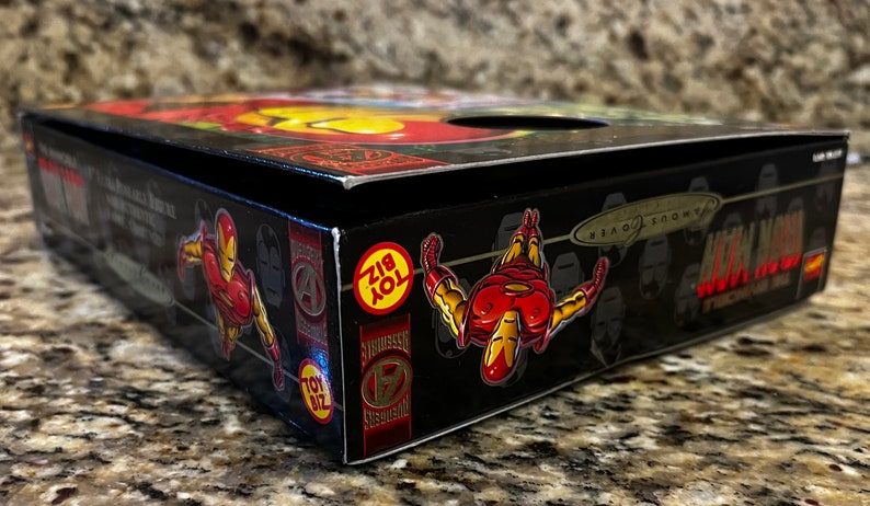 May include: A black box with a red and yellow Iron Man figure on the side. The box has the words "Iron Man" and "Toy Biz" on it.