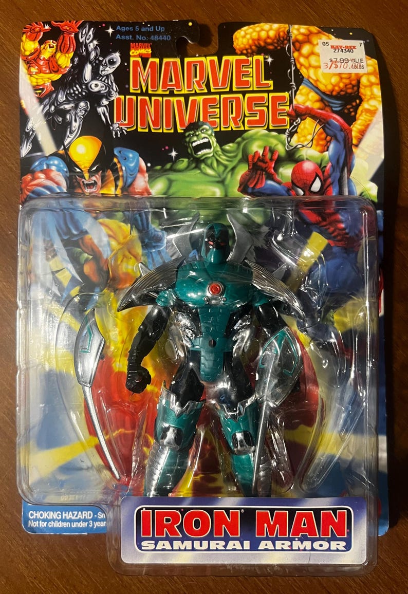 May include: A plastic package containing an action figure of Iron Man in a green and silver Samurai Armor. The figure is posed with a sword in its hand. The package has a red, white, and blue background with the words "Marvel Universe" and "Iron Man Samurai Armor" printed on it.