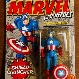 May include: A Captain America action figure in its original packaging. The packaging features the Marvel Super Heroes logo and a comic book style illustration of Captain America. The figure is blue, red, and white, with a shield and shield launcher.