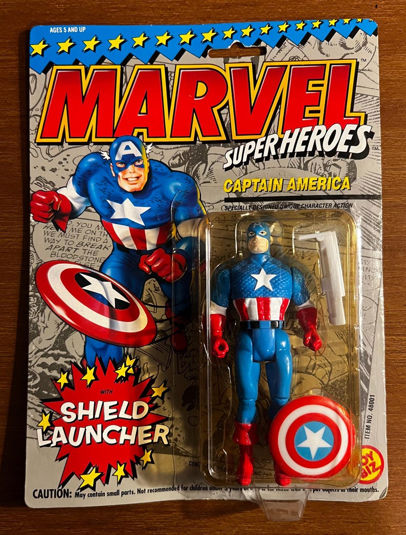 May include: A Captain America action figure in its original packaging. The packaging features the Marvel Super Heroes logo and a comic book style illustration of Captain America. The figure is blue, red, and white, with a shield and shield launcher.