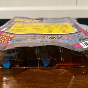 May include: A plastic blister pack containing a Fantastic Four action figure. The packaging is pink, gray, and white with the words "The Thing" and "Collect them all! Fantastic Four" printed on it. The figure is not visible in the packaging.