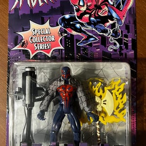 May include: A black and red Spider-Man 2099 action figure with a yellow and black axe weapon. The figure is packaged in a plastic blister pack with a purple and black background. The packaging features the Marvel logo and the text "The Amazing Spider-Man" and "Special Collector Series!"