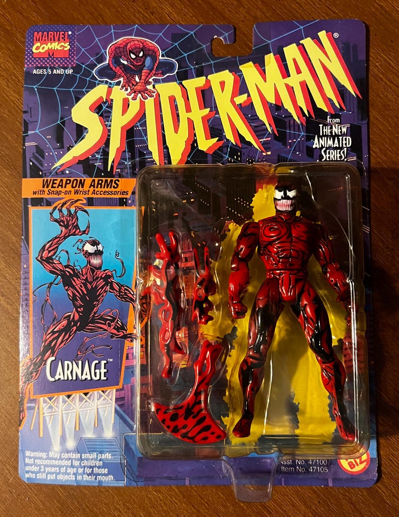 May include: Carnage action figure from the Spider-Man animated series. The figure is red and black with a white spider symbol on the chest. The figure comes with weapon arms and snap-on wrist accessories. The packaging features a cartoon image of Spider-Man and the text "Weapon Arms with Snap-on Wrist Accessories".