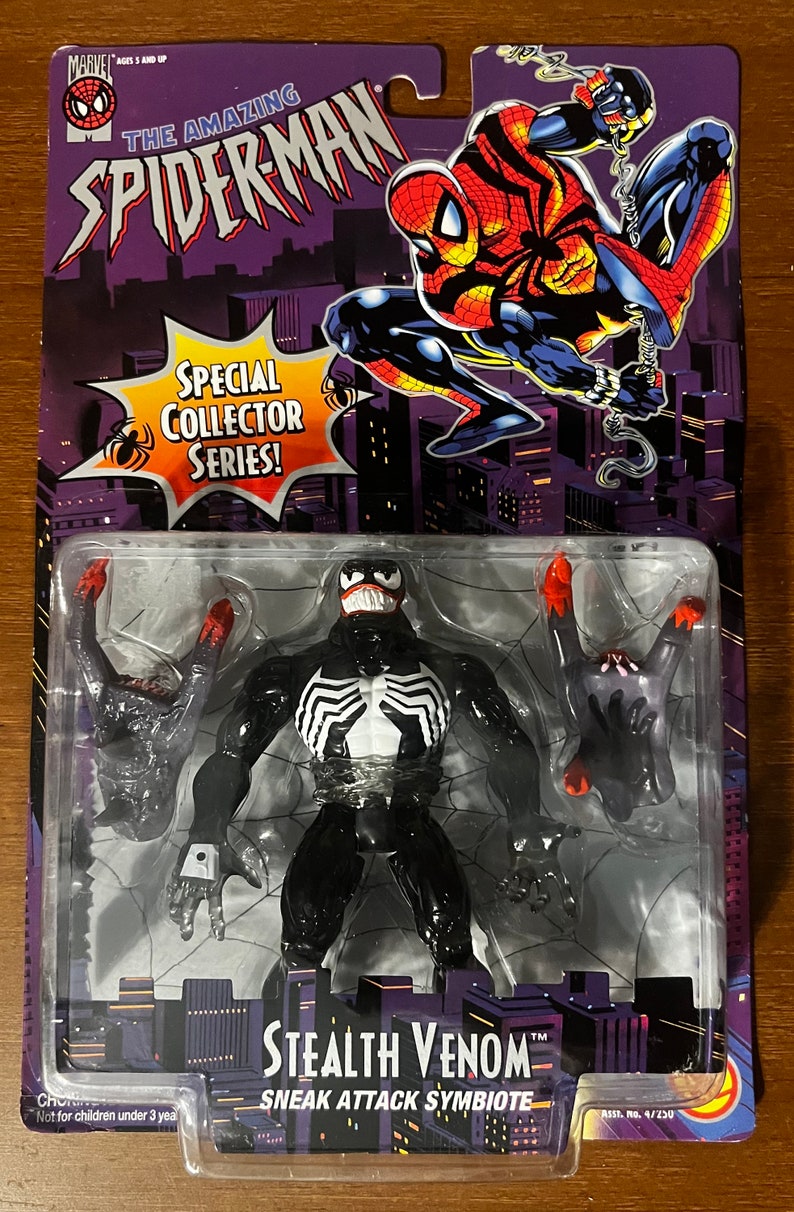 Puede incluir: Una figura de acci&oacute;n en blanco y negro de Venom, un personaje de Marvel Comics, con un traje de sigilo. La figura est&aacute; en pose con los brazos extendidos y la boca abierta en una mueca amenazante. La figura est&aacute; empaquetada en un bl&iacute;ster de pl&aacute;stico con un respaldo de cart&oacute;n. El respaldo presenta una imagen roja y azul de Spider-Man, el texto "The Amazing Spider-Man", y las palabras "Special Collector Series!" La figura est&aacute; etiquetada como "Stealth Venom" y "Sneak Attack Symbiote".