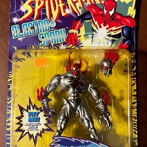 May include: A silver and red action figure of Spider-Man with a sparking chest. The figure is packaged in a plastic blister pack with a yellow background and the words "Electro Spark" on the front. The figure is part of the Marvel Comics line of toys.