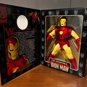 May include: A red and yellow action figure of Iron Man, the Invincible, in a box with a black background and a gold border. The box has a picture of Iron Man on the front and the words "The Invincible Iron Man" on the bottom.