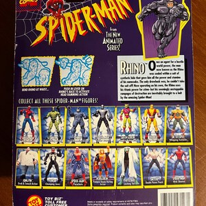 May include: Back of a Spider-Man action figure package featuring the Rhino character from the animated series. The package includes images of various Spider-Man figures and text describing the Rhino's origin and abilities. The package is purple and yellow.