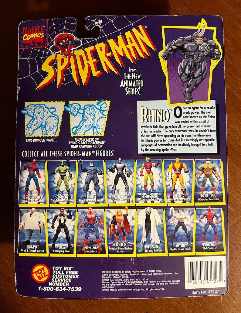 May include: Back of a Spider-Man action figure package featuring the Rhino character from the animated series. The package includes images of various Spider-Man figures and text describing the Rhino's origin and abilities. The package is purple and yellow.