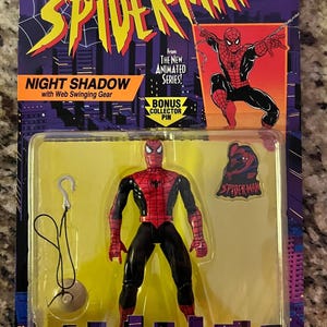 May include: A red and black Spider-Man action figure with web-swinging gear. The figure is packaged in a plastic blister pack with a yellow background. The packaging features the words "Spider-Man" and "Night Shadow" in large, bold letters. The packaging also includes a bonus collector pin.