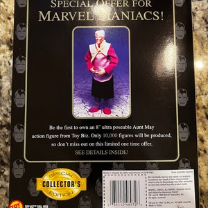 May include: A special collector's edition 8-inch Aunt May action figure from Toy Biz. The figure is posed with her hands clasped in front of her. She is wearing a red and white dress with a yellow scarf. The packaging features a black background with the words "Special Offer for Marvel Maniacs!" in white text. The back of the packaging includes a description of the figure and a toll-free customer service number.