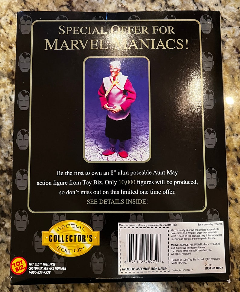 May include: A special collector's edition 8-inch Aunt May action figure from Toy Biz. The figure is posed with her hands clasped in front of her. She is wearing a red and white dress with a yellow scarf. The packaging features a black background with the words "Special Offer for Marvel Maniacs!" in white text. The back of the packaging includes a description of the figure and a toll-free customer service number.