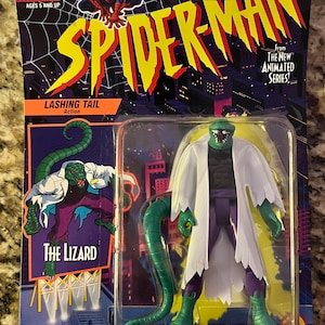 May include: A green and purple action figure of The Lizard from the Spider-Man animated series. The figure has a long green tail and is wearing a white lab coat. The packaging is purple and features the Spider-Man logo. The text on the packaging reads "Lashing Tail Action" and "The Lizard".