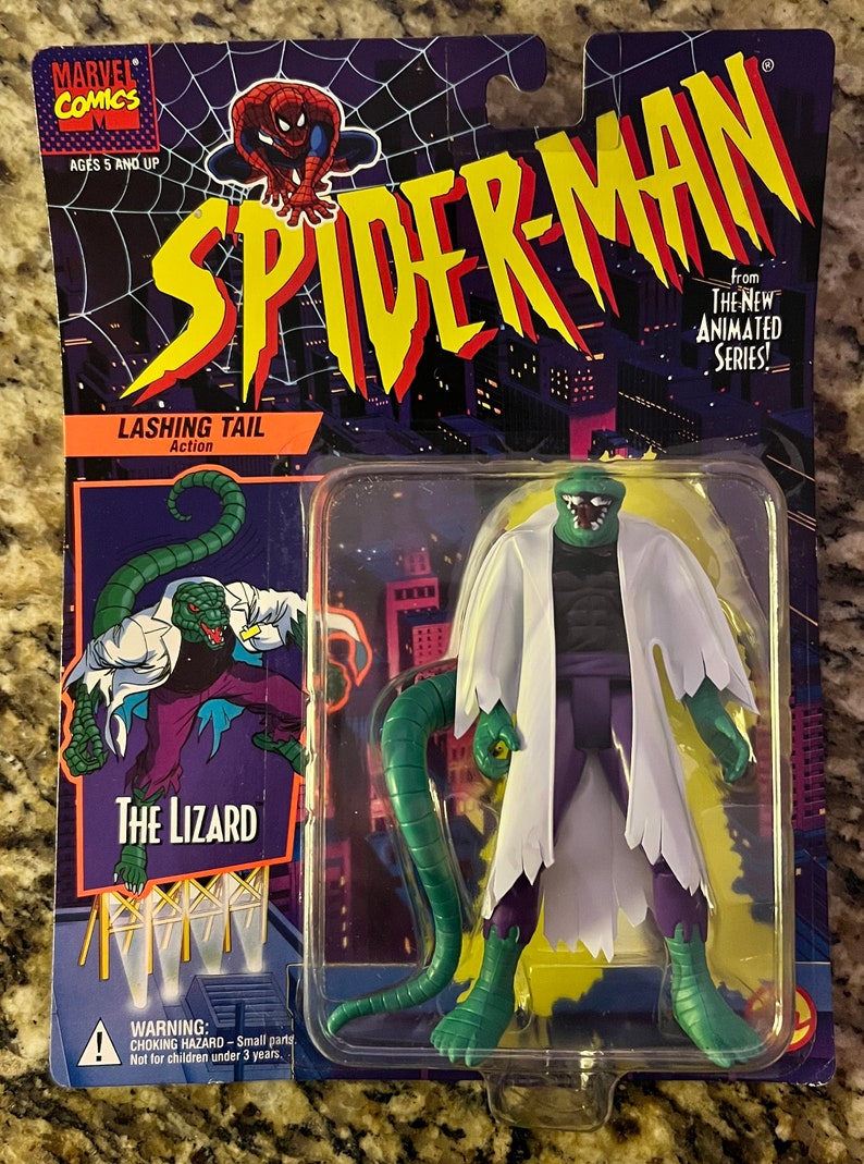 May include: A green and purple action figure of The Lizard from the Spider-Man animated series. The figure has a long green tail and is wearing a white lab coat. The packaging is purple and features the Spider-Man logo. The text on the packaging reads "Lashing Tail Action" and "The Lizard".