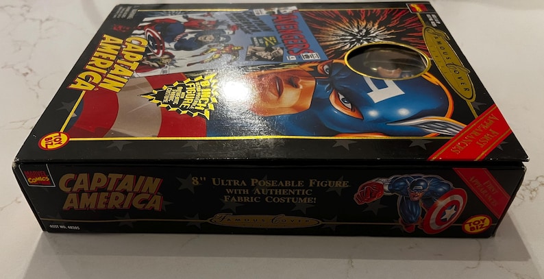 May include: A black box featuring Captain America artwork. The box includes the text "Captain America" and "8 inch Ultra Poseable Figure with Authentic Fabric Costume!" The box has a clear window showing the figure.
