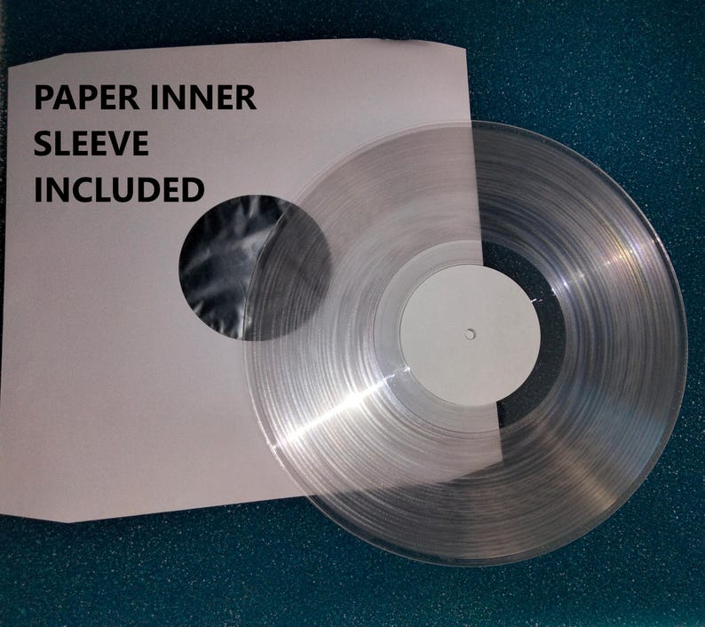 K&ouml;nnte beinhalten: Eine transparente Vinyl-Schallplatte mit wei&szlig;em Label, neben einer wei&szlig;en Papier-Innenh&uuml;lle. Auf der H&uuml;lle steht der Text "PAPER INNER SLEEVE INCLUDED". Die transparente Schallplatte l&auml;sst Licht durchscheinen.