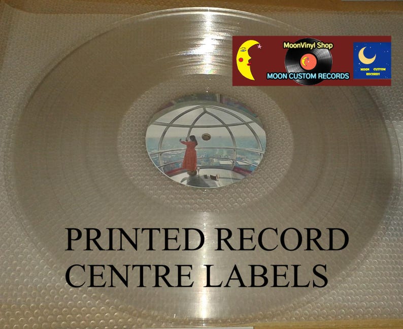 K&ouml;nnte beinhalten: Eine transparente Schallplatte mit reflektierender Oberfl&auml;che. Das Label in der Mitte zeigt ein Spiegelbild einer Person in einem orangefarbenen Kleid. Der Text "PRINTED RECORD CENTRE LABELS" ist darunter gedruckt. Ein Logo mit Mond und "MoonVinyl Shop" befindet sich oben rechts.