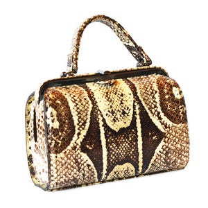 May include: A brown and cream snakeskin handbag with a top handle. The bag has a clasp closure and a rectangular shape.
