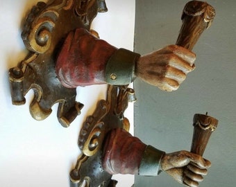 May include: Two ornate wall sconces with carved wooden hands holding wooden candle holders. The sconces are painted in shades of brown, gold, and green.