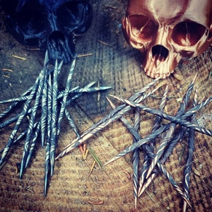 May include: Two sets of twisted metal needles, one set is silver and the other is copper. The needles are arranged in a starburst pattern. The needles are on a wooden surface.