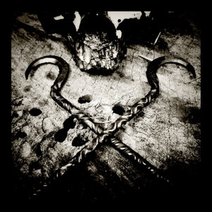 May include: Two black metal hooks with a twisted design are crossed over each other on a weathered wooden surface.