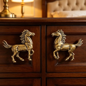 May include: Two brass-colored metal drawer pulls shaped like horses, mounted on a dark brown wooden cabinet. Each horse figure is depicted in a standing profile with a textured mane and tail, serving as a functional handle for the furniture drawers.