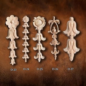 May include: Five intricately carved wooden decorative appliques in various floral and ornamental designs. Each piece is a light wood color and features detailed carvings. The appliques are labeled D-23 through D-27.