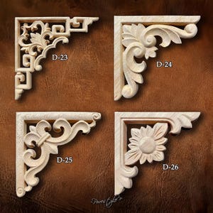 Puede incluir: Cuatro escuadras de esquina de madera sin pintar con intrincados diseños tallados. Cada escuadra presenta un patrón único, incluyendo motivos florales y geométricos. Las escuadras están etiquetadas D-23, D-24, D-25 y D-26, sobre un fondo marrón.