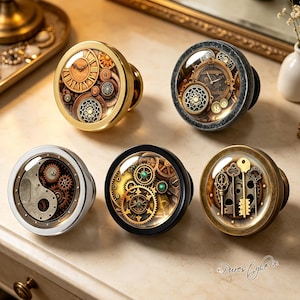 May include: Five circular cabinet knobs featuring intricate mechanical gear and key designs under glass domes. The knobs have varied metallic finishes including polished gold, dark textured gray, silver, matte black, and antique bronze.