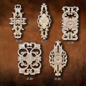 May include: Five intricately carved wooden decorative appliques. Each applique features floral and scroll designs. The appliques are labelled D-26, D-27, D-28, D-29, and D-30. The appliques are light in colour and set against a brown background.