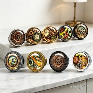 May include: A collection of nine circular cabinet knobs featuring diverse designs under glass domes. The patterns include intricate clockwork gears, mechanical watch components, compass motifs, and metallic finishes in silver, bronze, and black tones.