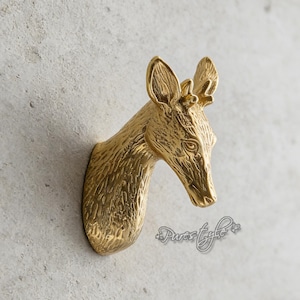May include: A gold-colored deer head wall mount. The deer head is sculpted with detailed features, including antlers, ears, and facial details. The mount is attached to a light gray wall.