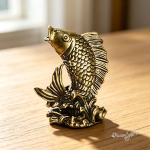 May include: A small, antique-style brass figurine of a fish leaping from stylized waves. The metal has a dark, weathered patina in the crevices of the scales and fins, contrasting with the polished, golden-toned highlights on the raised surfaces.