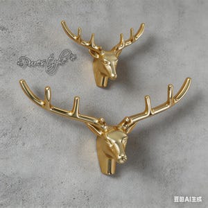 May include: Two gold-coloured deer head wall decorations. The deer heads are facing forward with detailed antlers. The wall decor is mounted on a grey textured wall. The text "Pure light" is in the upper left corner.