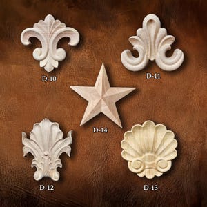 May include: Five unfinished wooden decorative carvings. The carvings include a fleur-de-lis, a star, and shell-like shapes. Each carving is labeled with a "D-" followed by a number. The carvings are displayed on a brown background.