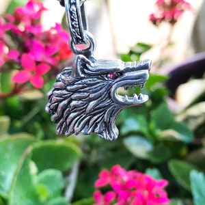 May include: Silver wolf's head pendant with red eyes, hanging from a silver chain. The pendant is detailed with fur and sharp teeth.