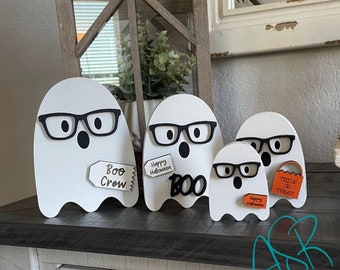 May include: Four white wooden ghost figures with black glasses and black eyes. One ghost has a tag that says "Boo Crew", another says "Happy Halloween Boo", and another says "Trick or Treat". Halloween decor.