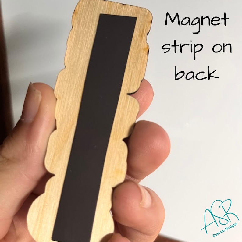 May include: Wooden cutout with a magnetic strip on the back. The cutout is shaped like a series of circles and has a natural wood finish. The text "Magnet strip on back" is written on the white background behind the cutout. The text "ASR Custom Designs" is written in teal on the bottom right corner of the image.