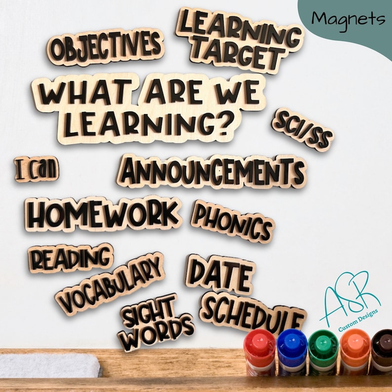 May include: A set of wooden classroom magnets with black lettering. The magnets include words like "Learning Target", "What Are We Learning?", "Announcements", "Homework", "Phonics", "Reading", "Vocabulary", "Date", "Schedule", "Sight Words", "Objectives", "I Can", and "Sci/SS".