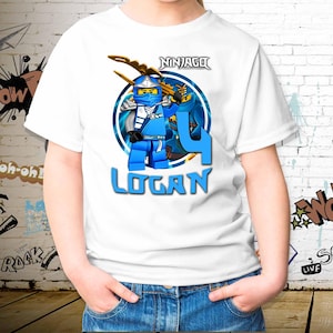 Puede incluir: Camiseta blanca con un diseño de personaje Lego Ninjago azul, el número 4 y el nombre "Logan" en azul. La camiseta tiene cuello redondo y mangas cortas.