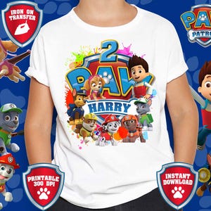 Pode incluir: T-shirt branca com um gráfico colorido dos personagens da Patrulha Pata, o número 2 e o nome "Harry". O design inclui o logotipo da Patrulha Pata e vários personagens da série.