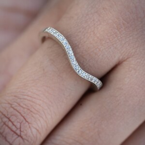 May include: A silver ring with a wavy band and a row of small clear stones.