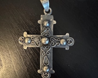 May include: A silver cross pendant with intricate details and a bail at the top. The cross has a textured surface and is decorated with small round beads.