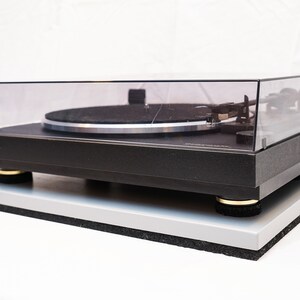 May include: A black Marantz turntable with a clear dust cover and a silver platter. The turntable is sitting on a gray platform with gold feet.