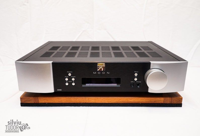 May include: A black and silver audio amplifier with a wood base. The amplifier has a silver knob on the right side and a display screen with the word "MOON" on it.