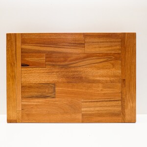 May include: A rectangular wooden cutting board with a natural wood finish. The board is made of multiple pieces of wood that have been joined together to create a unique pattern.