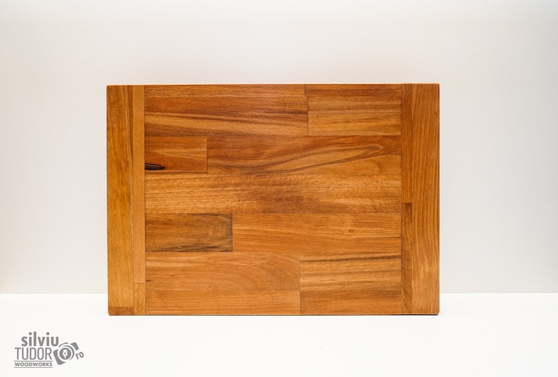 May include: A rectangular wooden cutting board with a natural wood finish. The board is made of multiple pieces of wood that have been joined together to create a unique pattern.