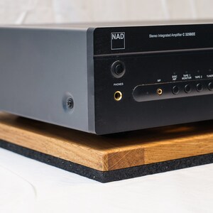 May include: A black stereo integrated amplifier with the text "NAD" and "Stereo Integrated Amplifier C 320BEE" on the front. The amplifier is sitting on a wooden platform with a black foam base.