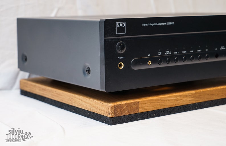 May include: A black stereo integrated amplifier with the text "NAD" and "Stereo Integrated Amplifier C 320BEE" on the front. The amplifier is sitting on a wooden platform with a black foam base.