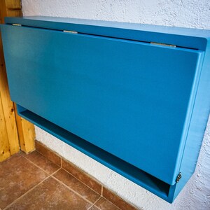 May include: A blue wall-mounted folding table with a shelf underneath. The table is closed and has a simple design.