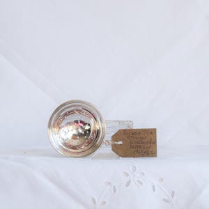 May include: A silver tea strainer with a tag attached. The strainer is round with a perforated bowl and a handle. The tag reads "Silver Tea Strainer, Nottingham, Sheffield, M6525".
